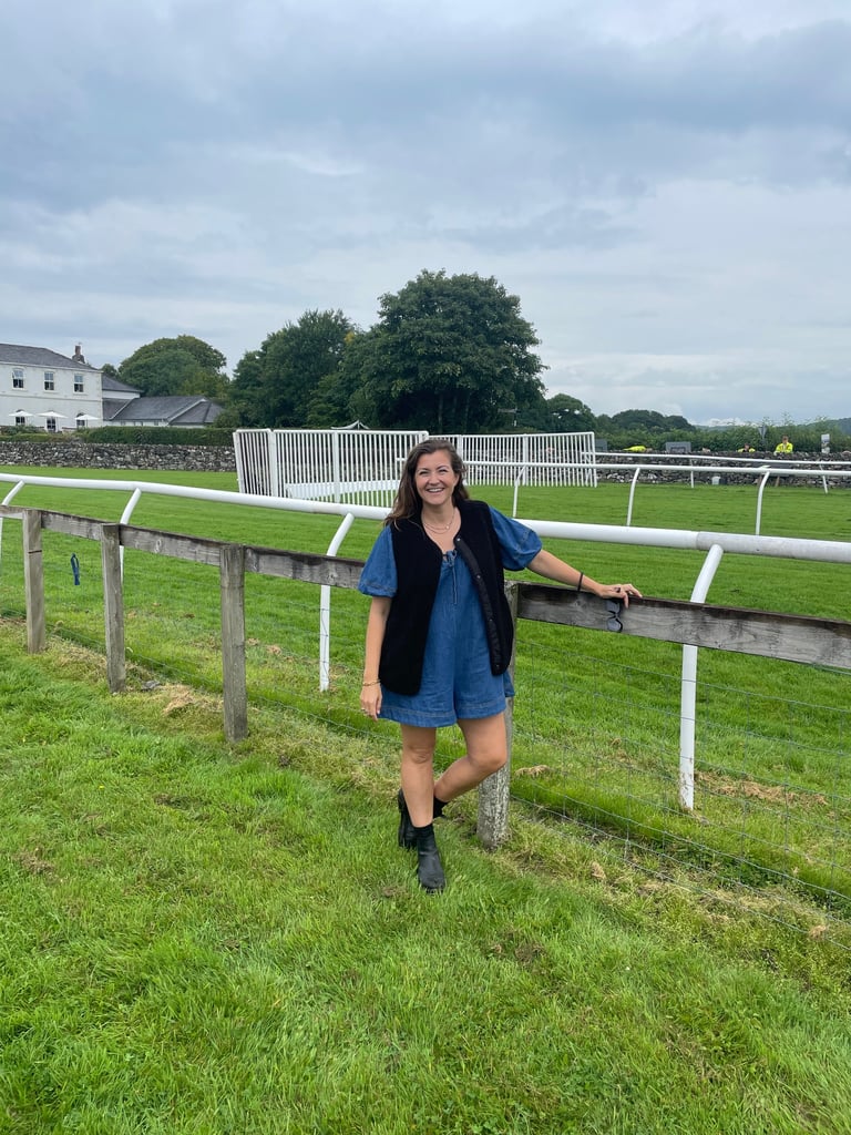 Woman standing in front of the horse racing track at Cartmel Racecourse.