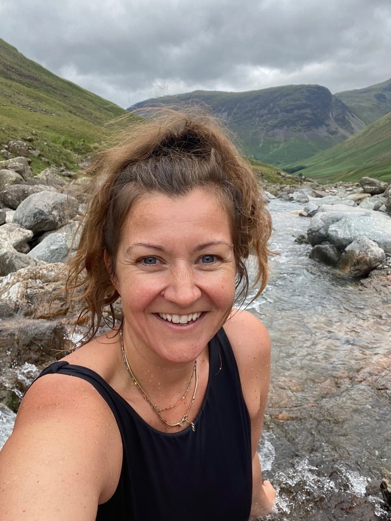 Woman sat in a waterfall at Great Gable in the Fairy pools in swimming costume. In the Lake District national park showing wild swimming.