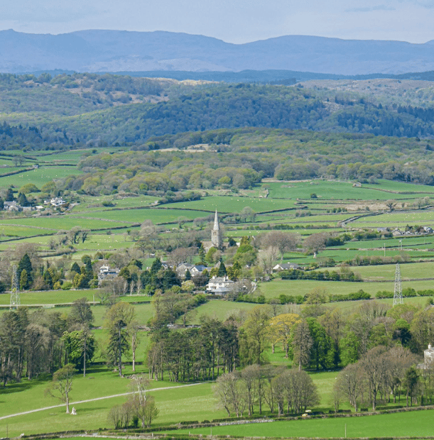 St Peter's Church in Field Broughton, the Lake District in the centre. Green grass and fields surround the church in Cartmel Valley