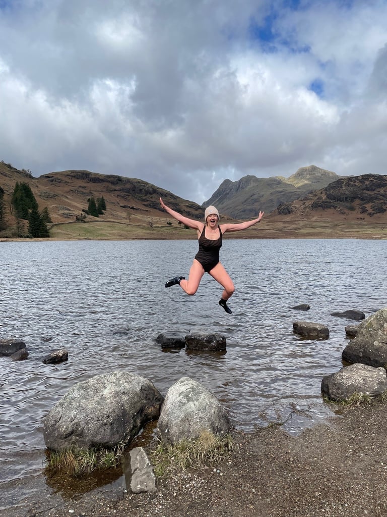 Host of The Pheasant Lodge Hannah jumping from a rock in Blea Tarn surrounded by Lake District mountains. A perfect lake district wild swimming spot