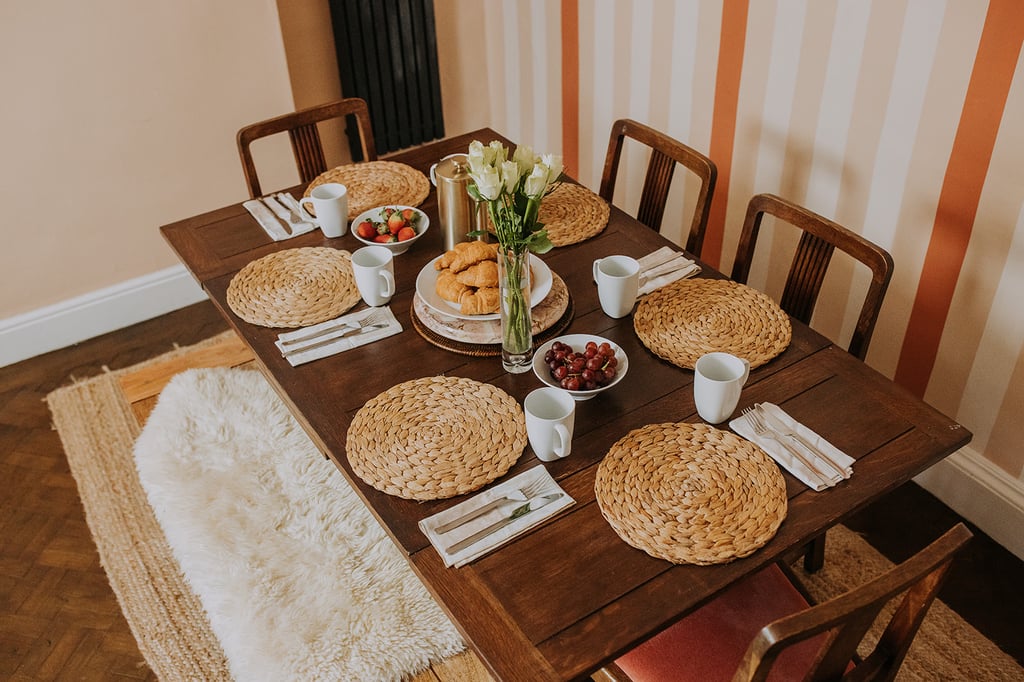 Dining table laid for six with croissants, fruit, mugs and woven placemats