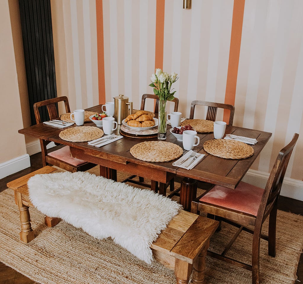 Dining table set for breakfast with croissants, mugs and a wooden bench